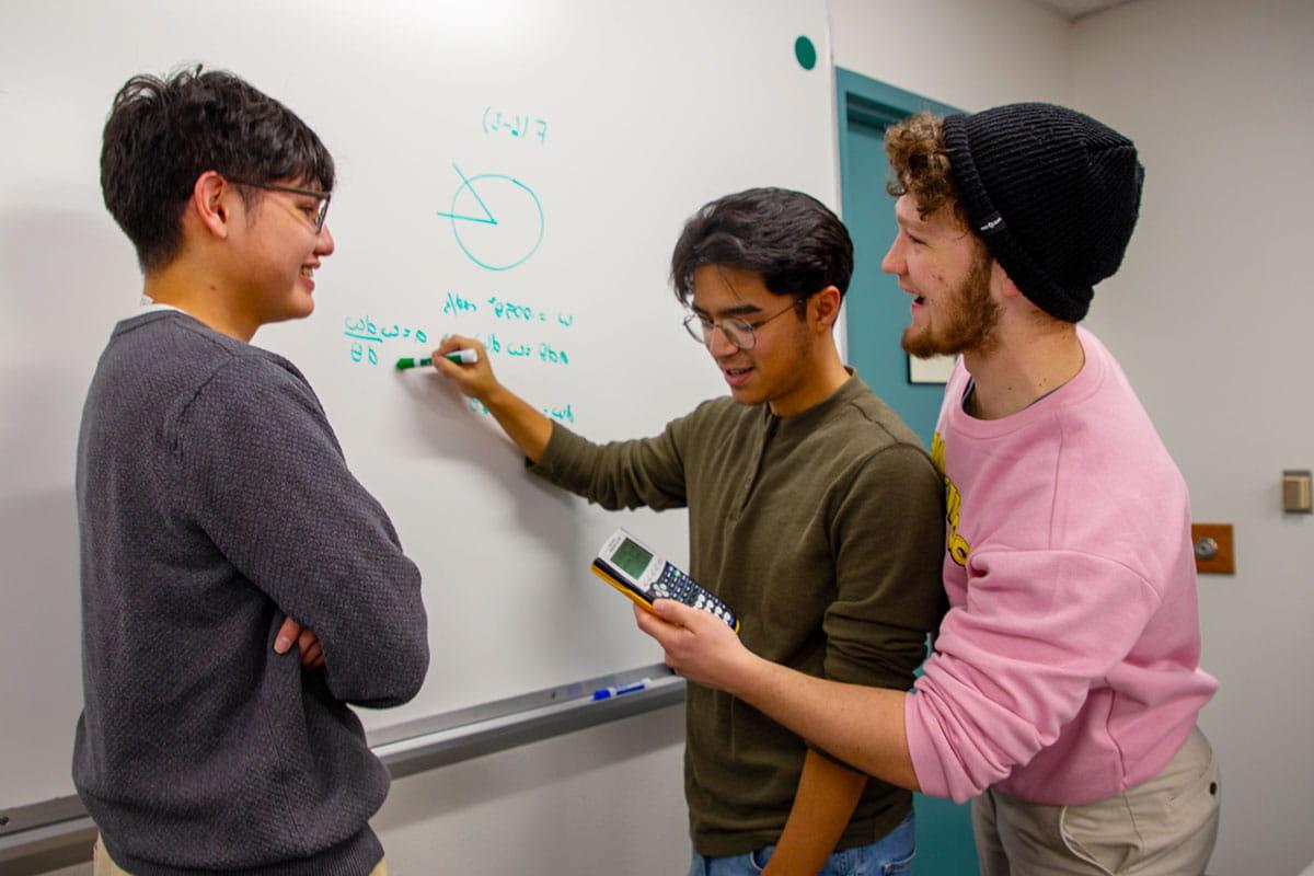 三个火博体育的学生正在白板上做一道数学题